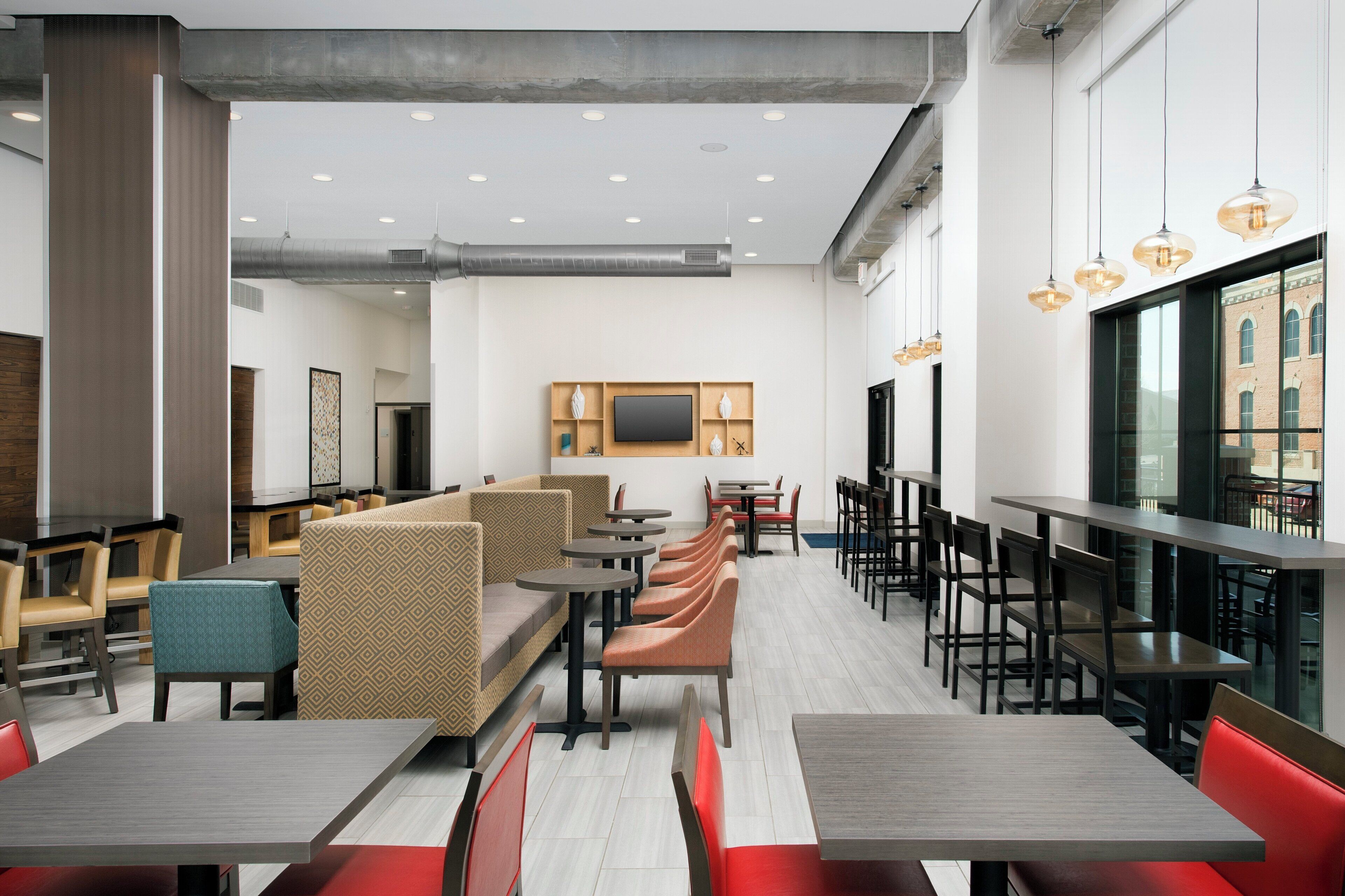 Interior de restaurante moderno com pé-direito alto, iluminação embutida e diversos tipos de assentos, incluindo cabines e mesas.