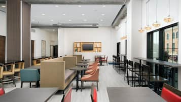 Interior de restaurante moderno com pé-direito alto, iluminação embutida e diversos tipos de assentos, incluindo cabines e mesas.