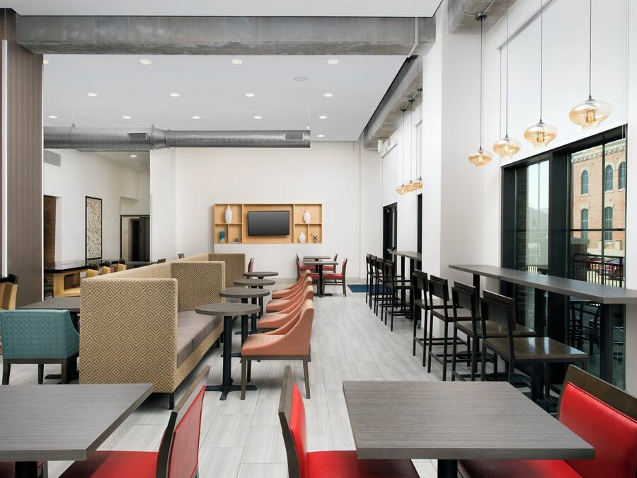 Interior de restaurante moderno com pé-direito alto, iluminação embutida e diversos tipos de assentos, incluindo cabines e mesas.