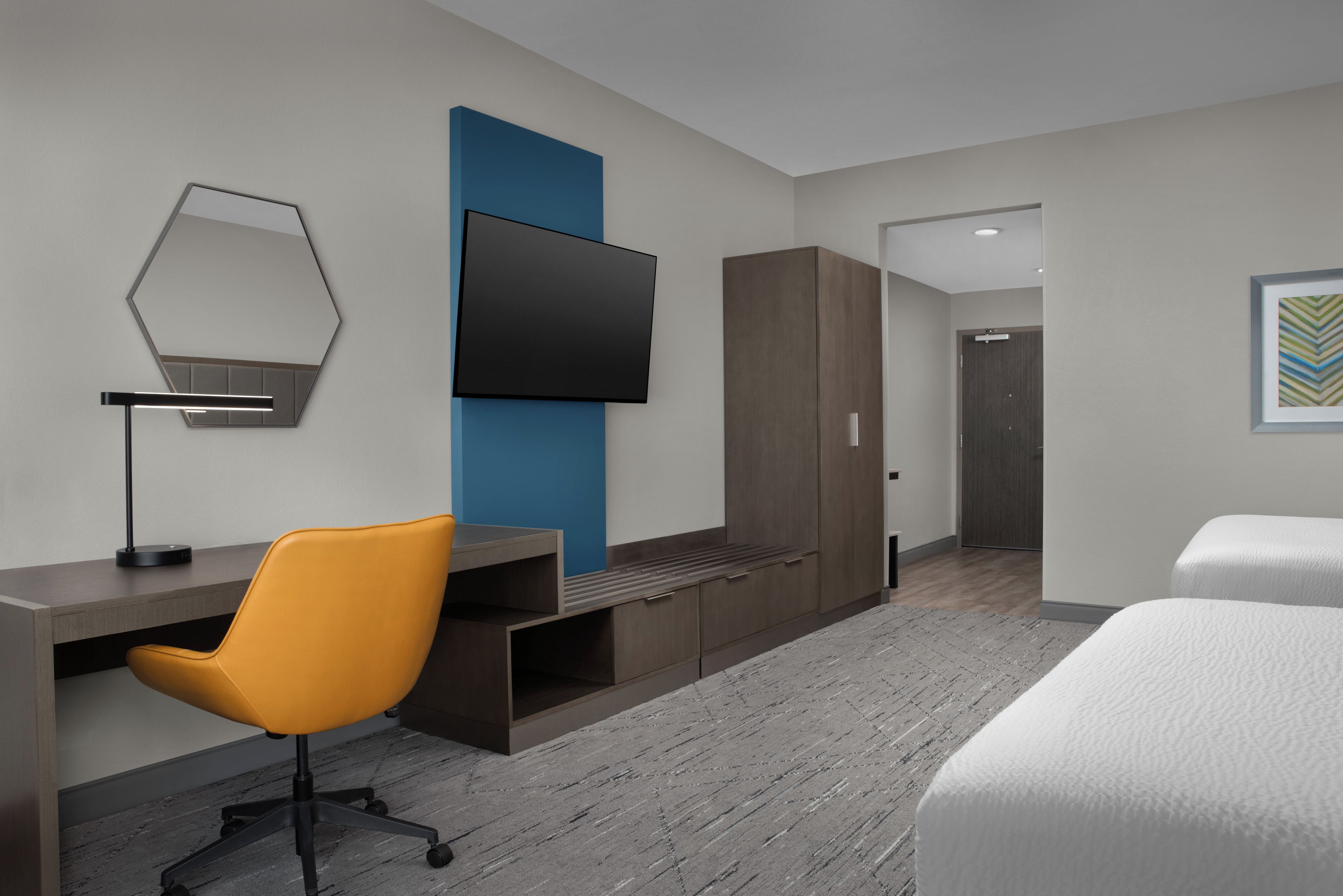 Een moderne hotelkamer met een bureau, stoel, kledingkast, bed en een wandgemonteerde flatscreen-tv.