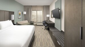 Quarto de hotel com uma cama grande, uma escrivaninha, uma cadeira, uma TV de tela plana e uma janela ampla com cortinas.