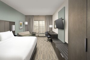 A hotel room with a large bed, a desk, a chair, a flat-screen TV, and a large window with curtains. - Holiday Inn Express Pensacola Downtown by IHG (Pensacola)