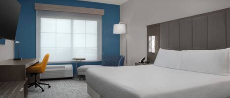 A hotel room with a large bed, a desk, a chair, a TV, and a window.