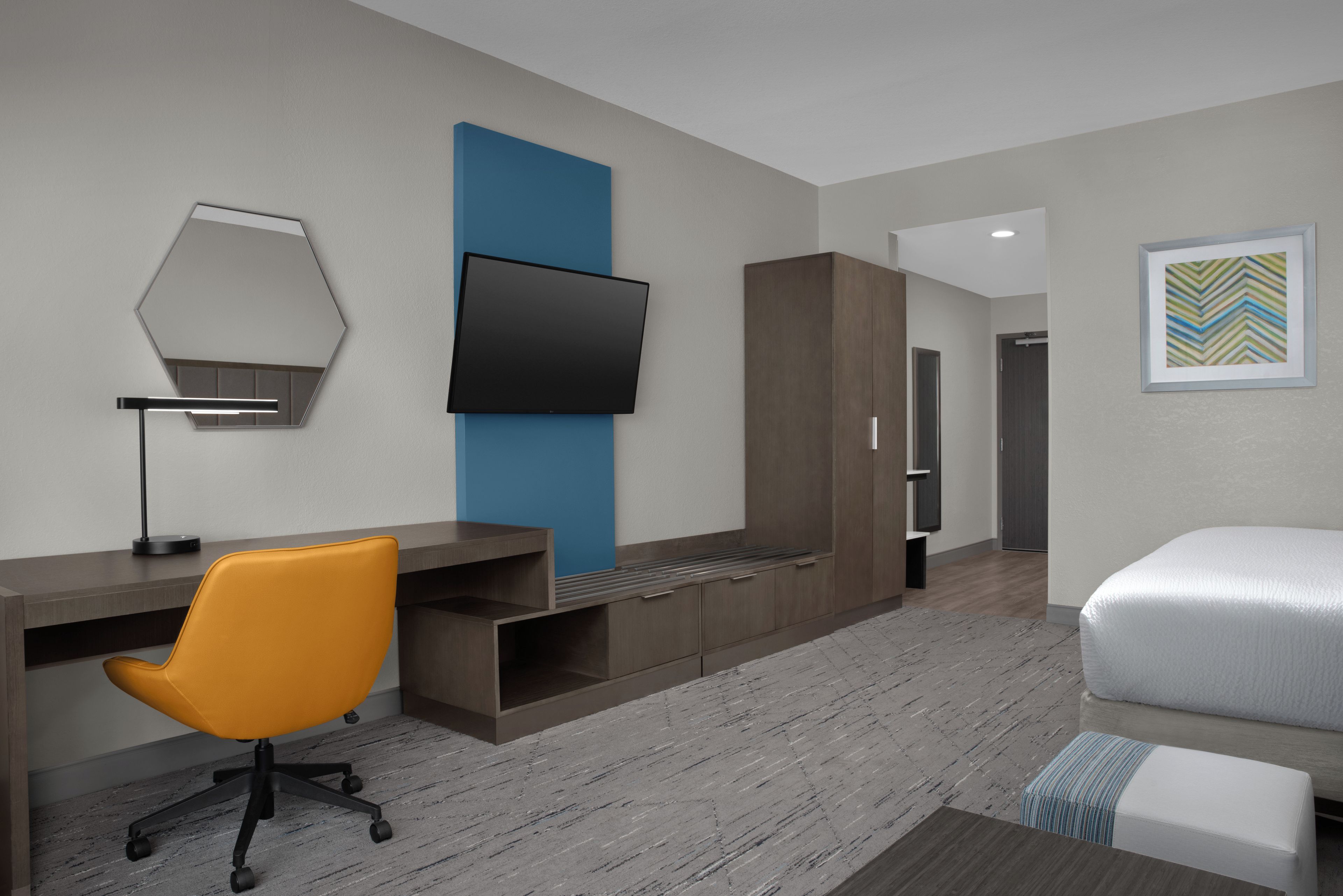 Camera d'albergo moderna con una scrivania, una sedia, un armadio e una TV a schermo piatto montata a parete.