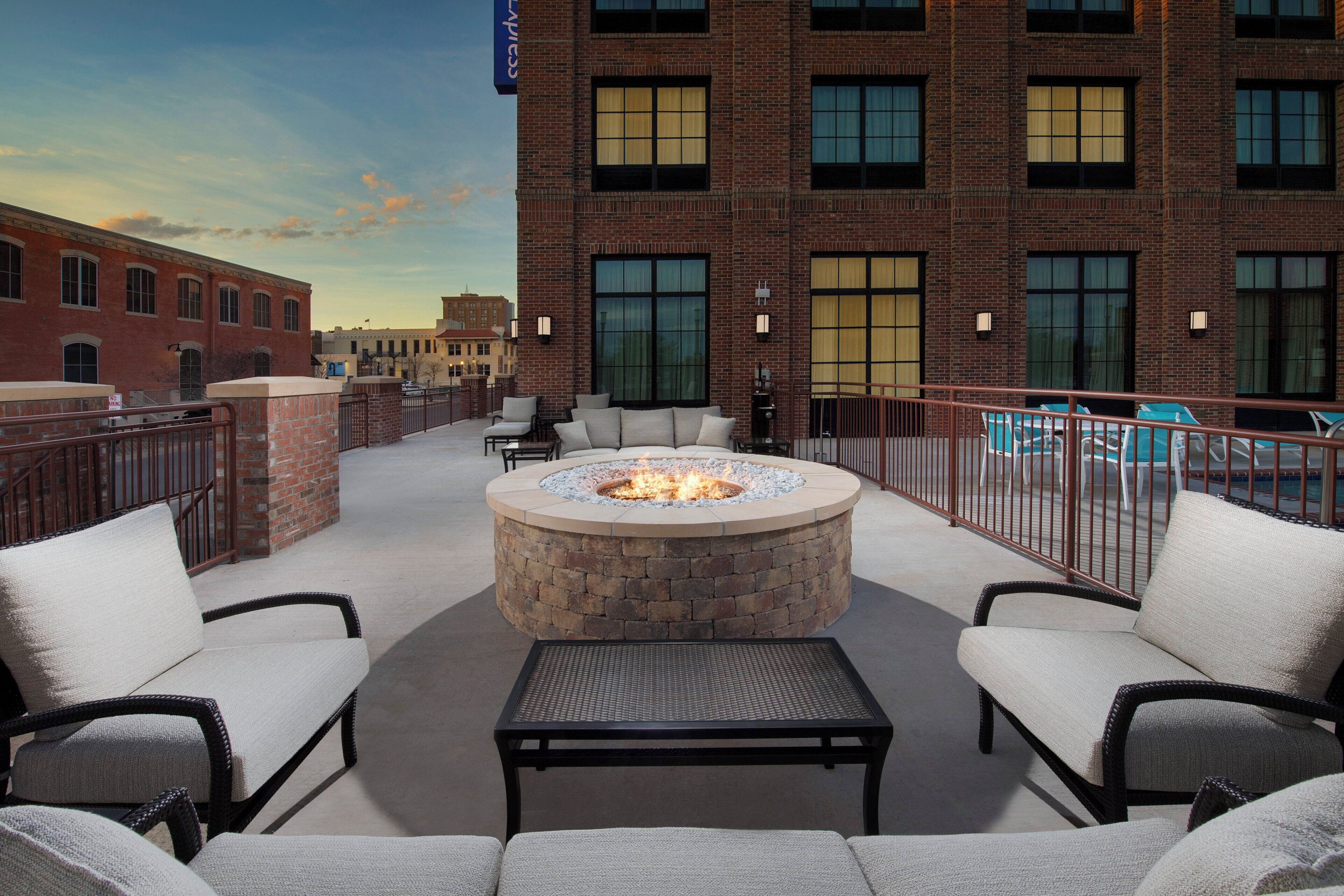 An outdoor seating area with a fire pit, chairs, and a view of a brick building.