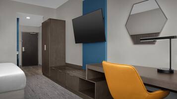 Ein modernes Hotelzimmer mit Bett, Schreibtisch, Stuhl, Flachbildfernseher und Spiegel.