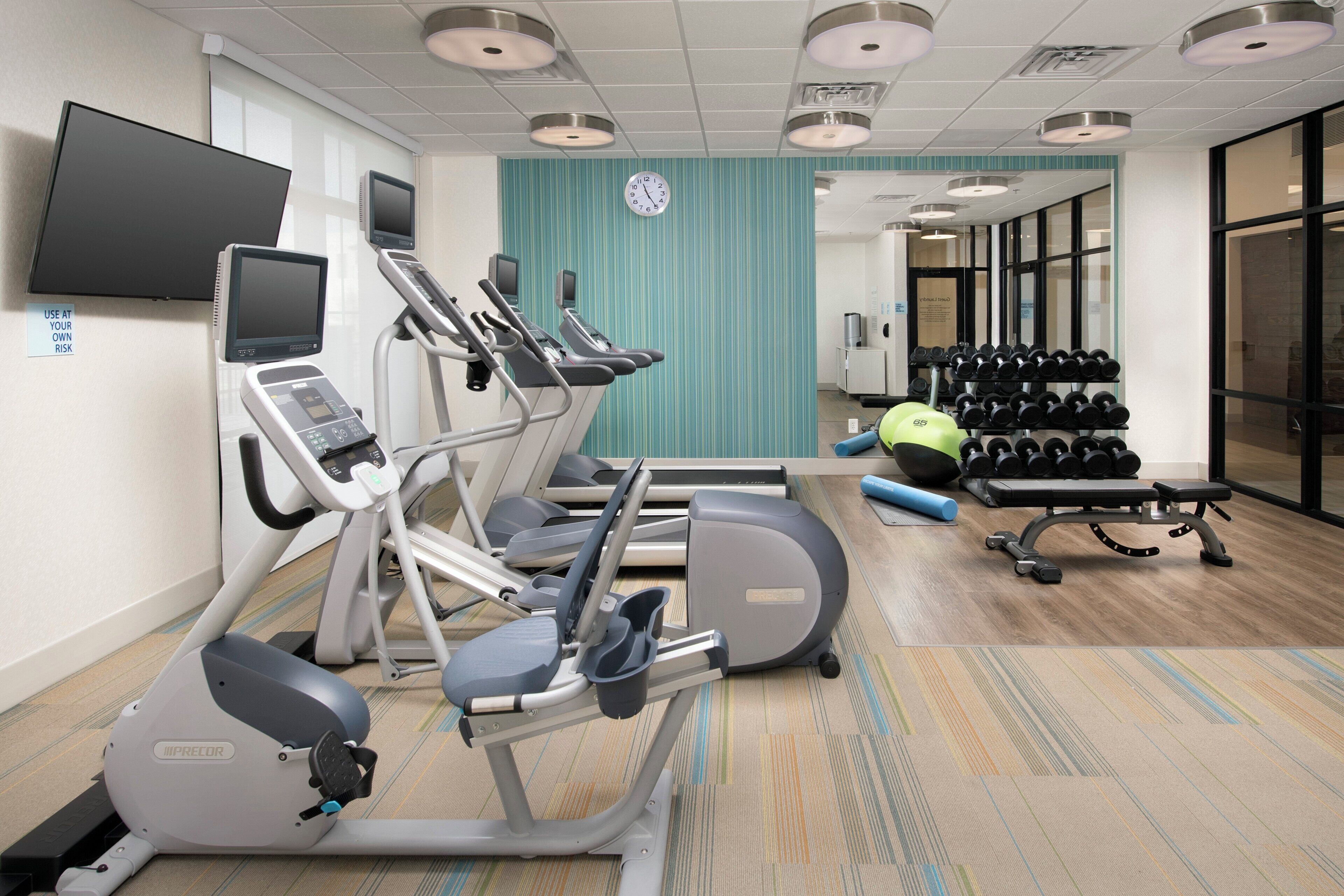 A fitness center with treadmills, an elliptical, a weight bench, and a rack of dumbbells.