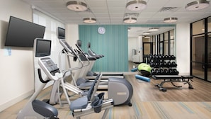 Un gimnasio con cintas de correr, elípticas, un banco de pesas y una estantería con mancuernas.