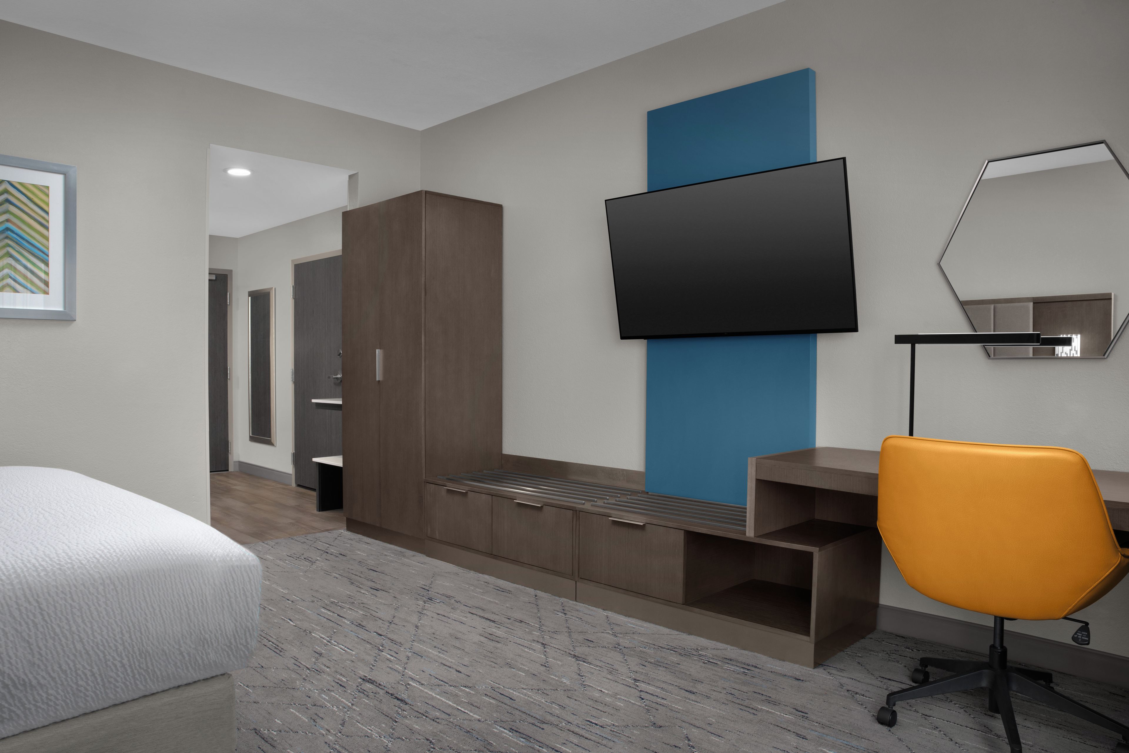 A modern hotel room with a bed, a desk, a chair, a TV, and a wardrobe.