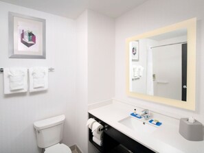 A modern bathroom with a toilet, sink, and large mirror. There are towels hanging on the wall and a framed picture above the toilet. - Holiday Inn Express Pensacola Downtown by IHG (Pensacola)
