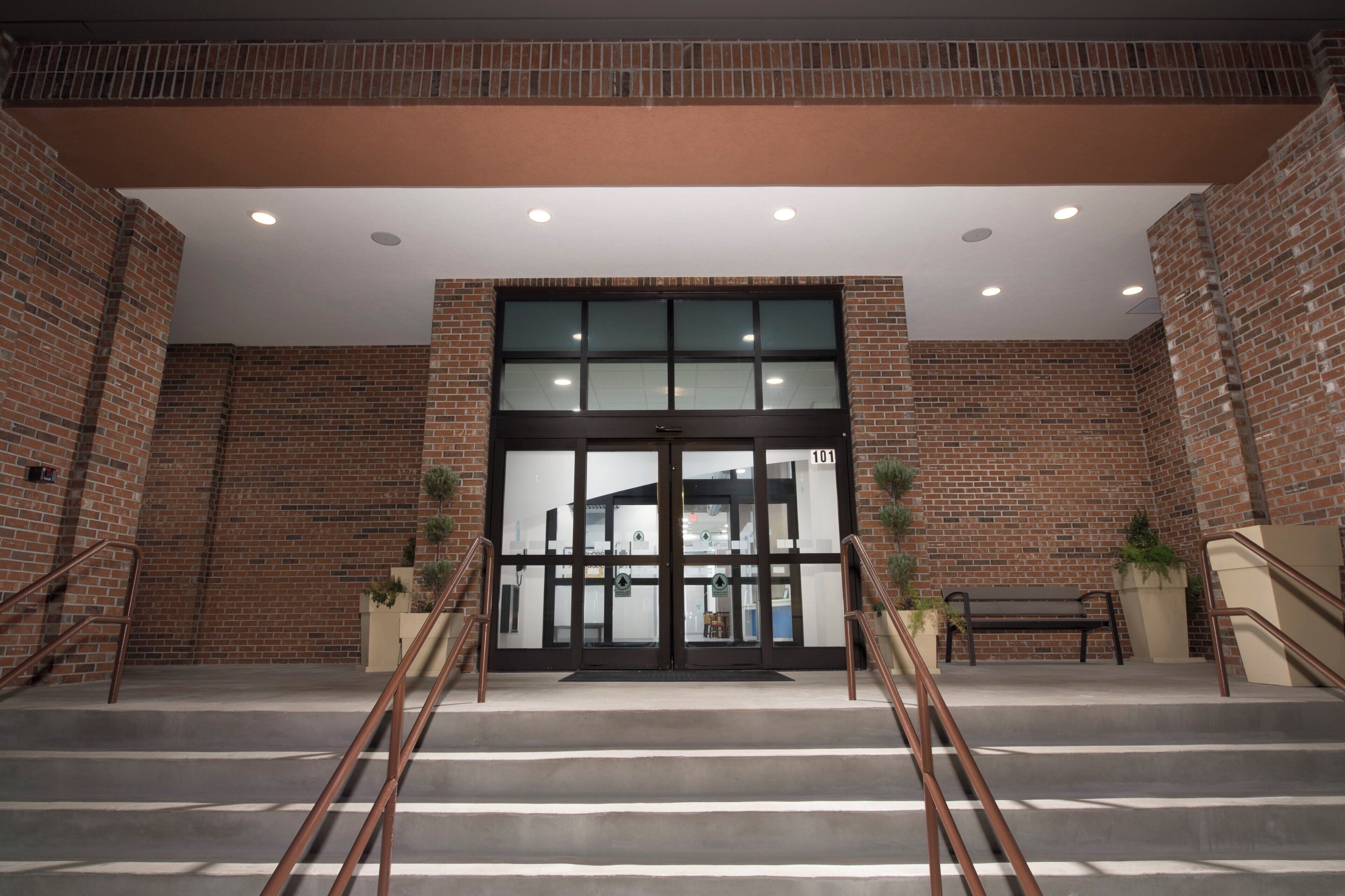 A building entrance with a brick facade, a glass door, and a staircase leading up.