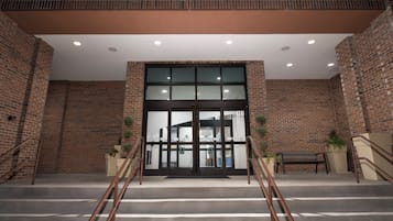 A building entrance with a brick facade, a glass door, and a staircase leading up.