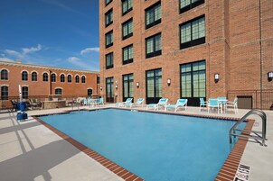 A swimming pool with lounge chairs and a brick building in the background.