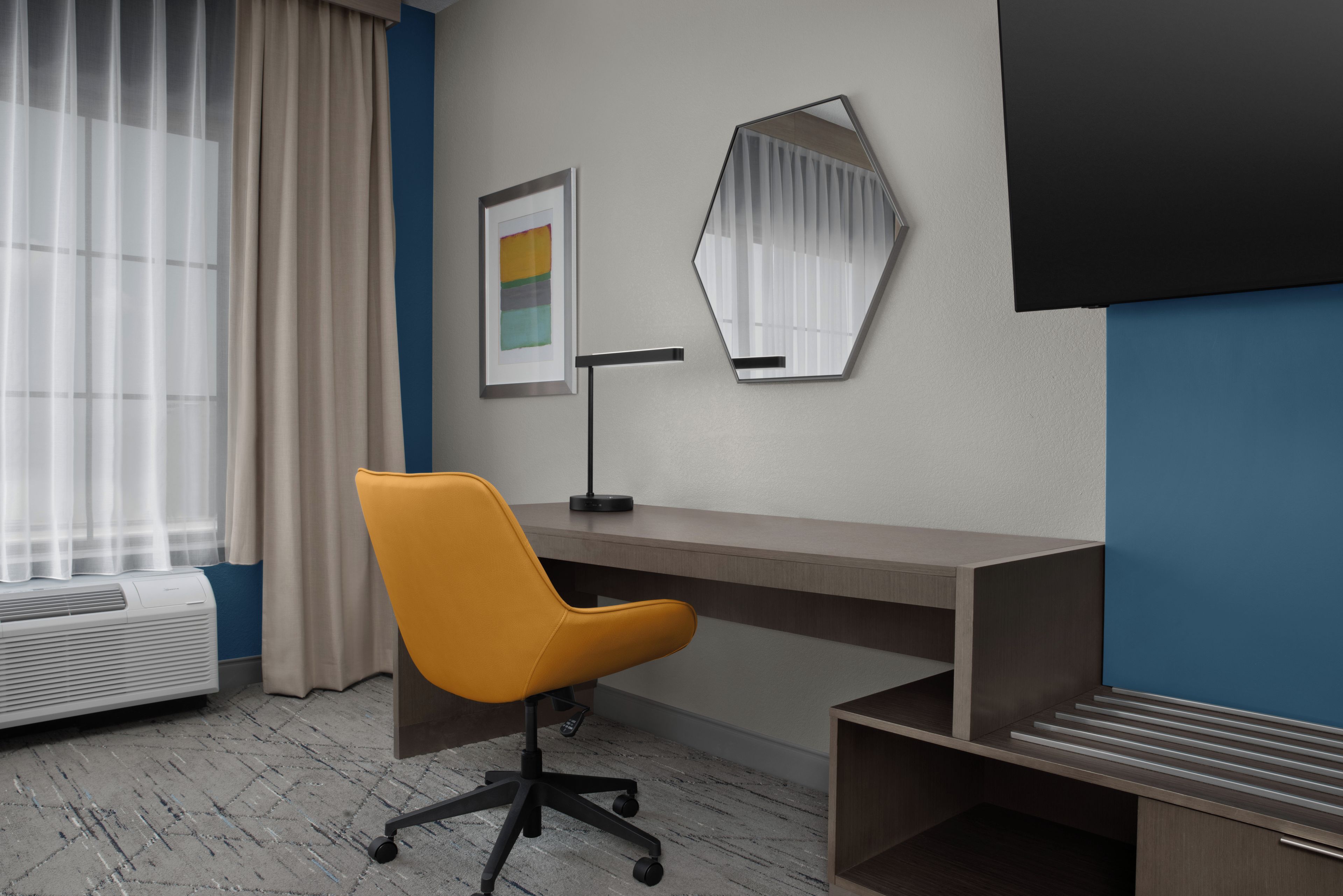 A modern office space with a desk, chair, air conditioning unit, and a large mirror.