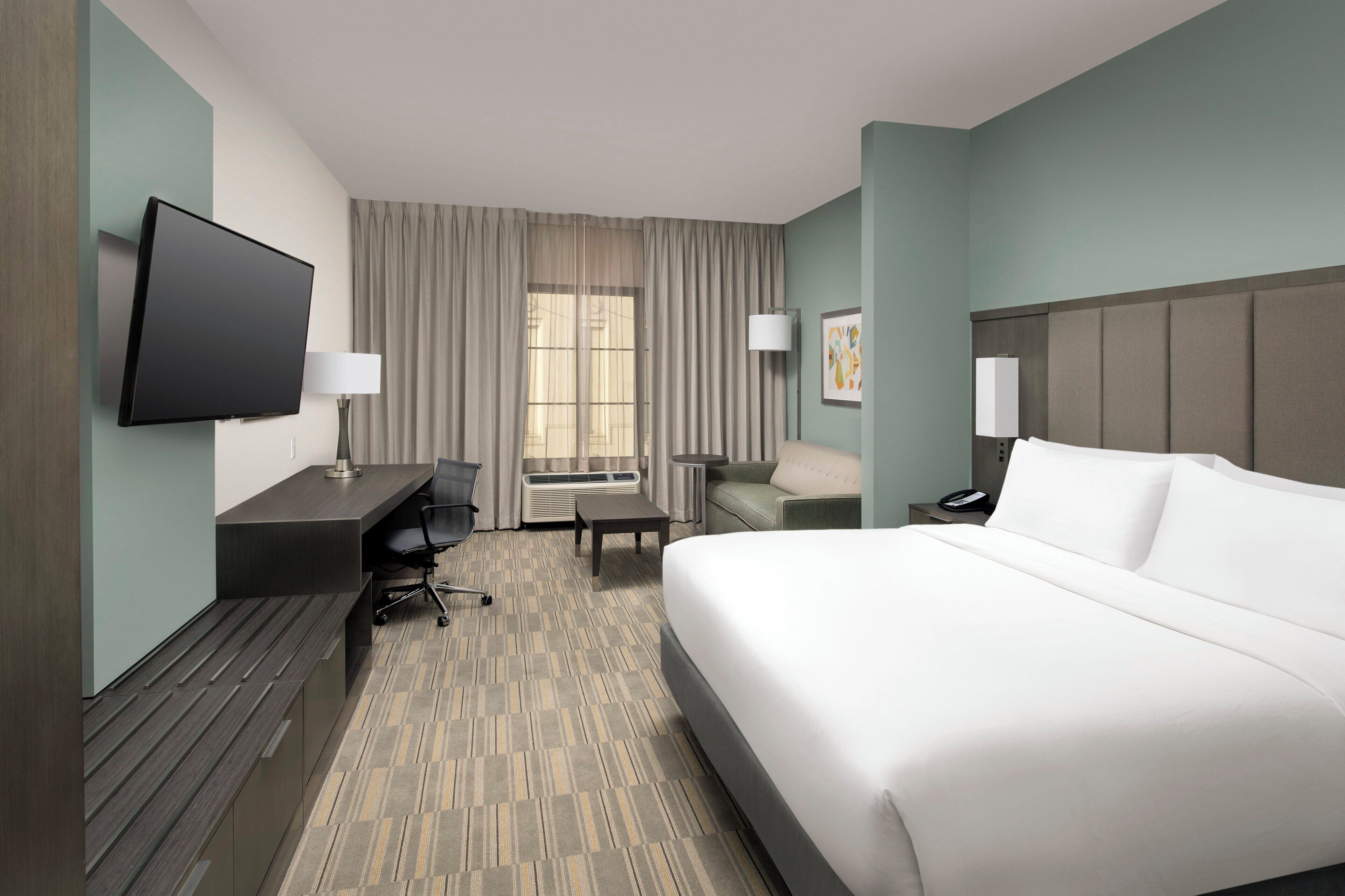 A hotel room with a bed, desk, chair, TV, and a window with curtains.