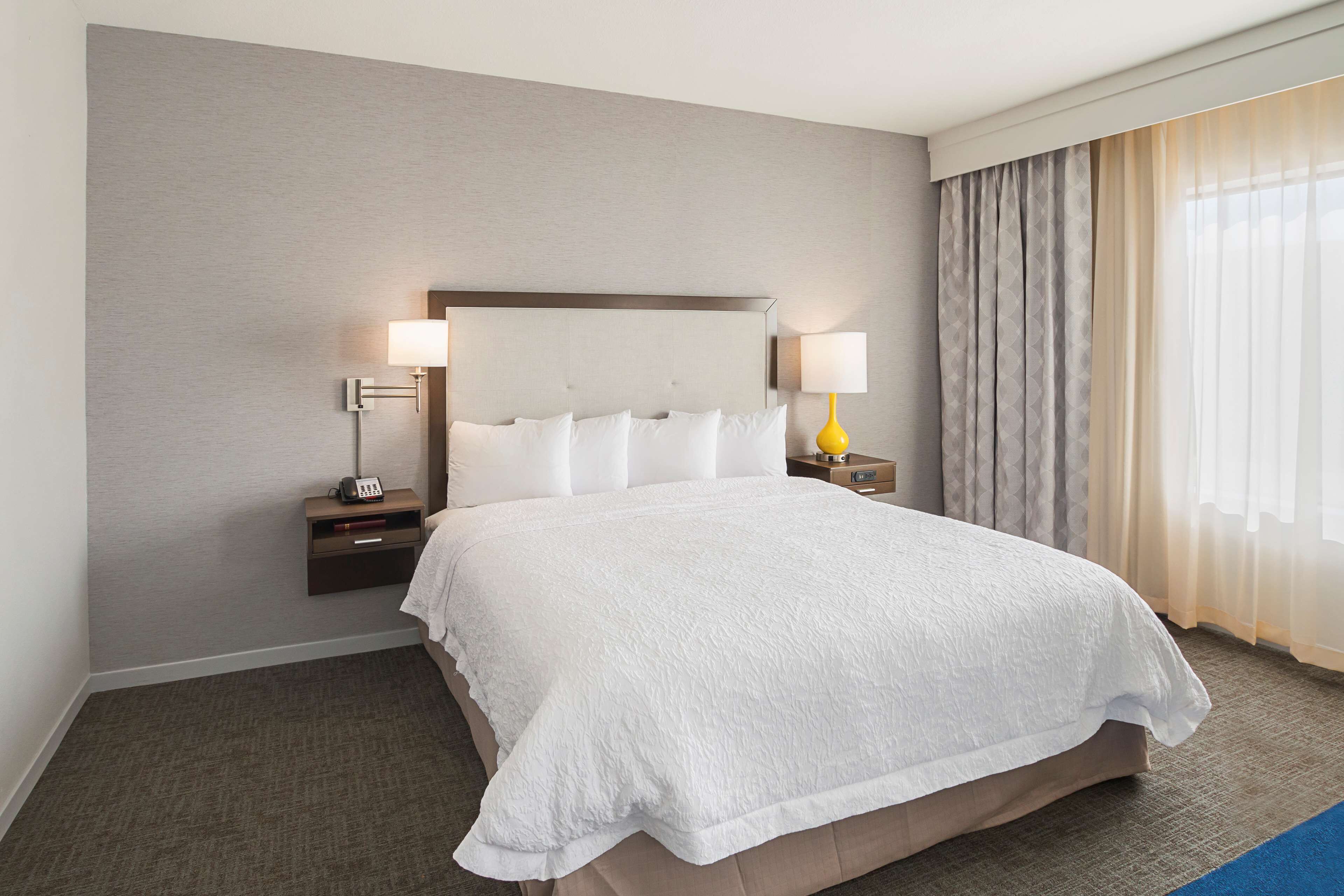 A hotel room with a large bed, two bedside tables with lamps, a nightstand with a radio, and a window with curtains.