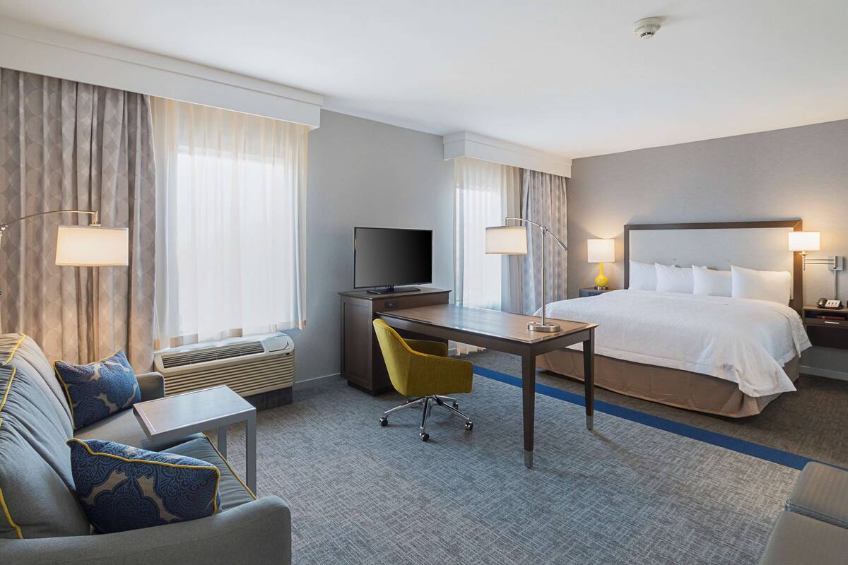 A hotel room with a bed, a desk, a chair, a television, and a window with curtains.