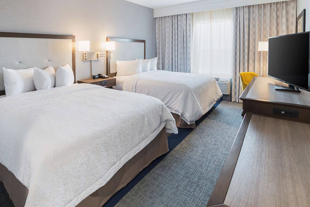 A hotel room with two beds, a TV, and a desk.