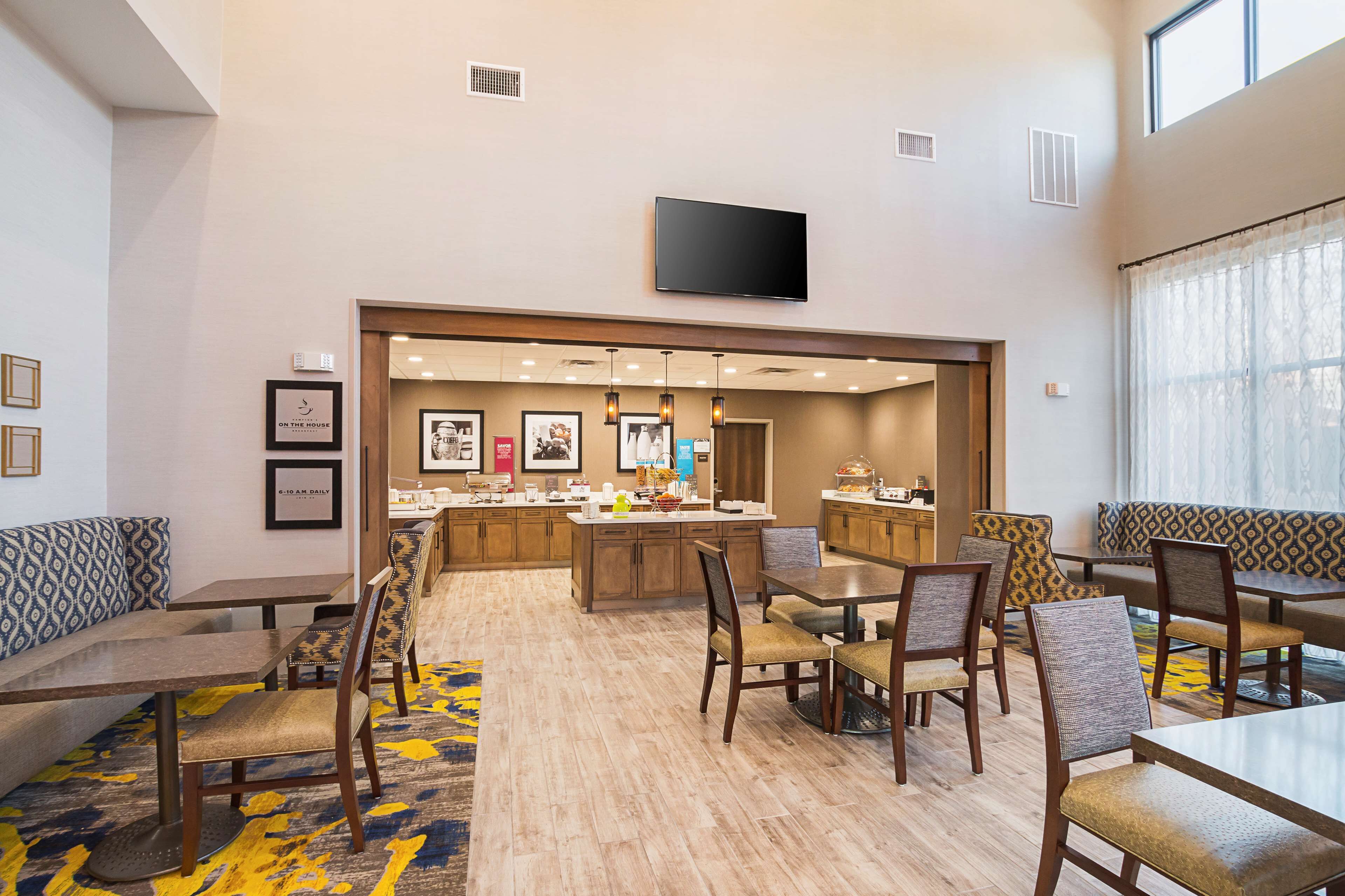 A hotel dining area with a central island, seating arrangements, and a television mounted on the wall.