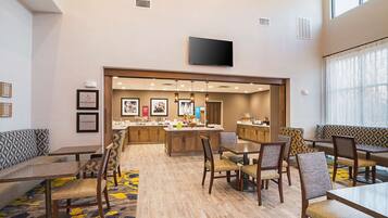A hotel dining area with a central island, seating arrangements, and a television mounted on the wall.