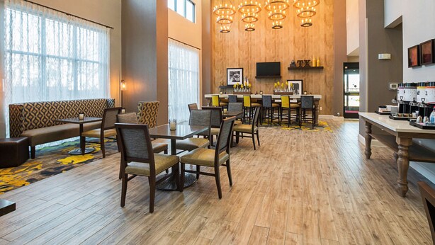A spacious lobby with a wooden floor, a seating area with a patterned sofa, and a bar with a flat-screen TV.