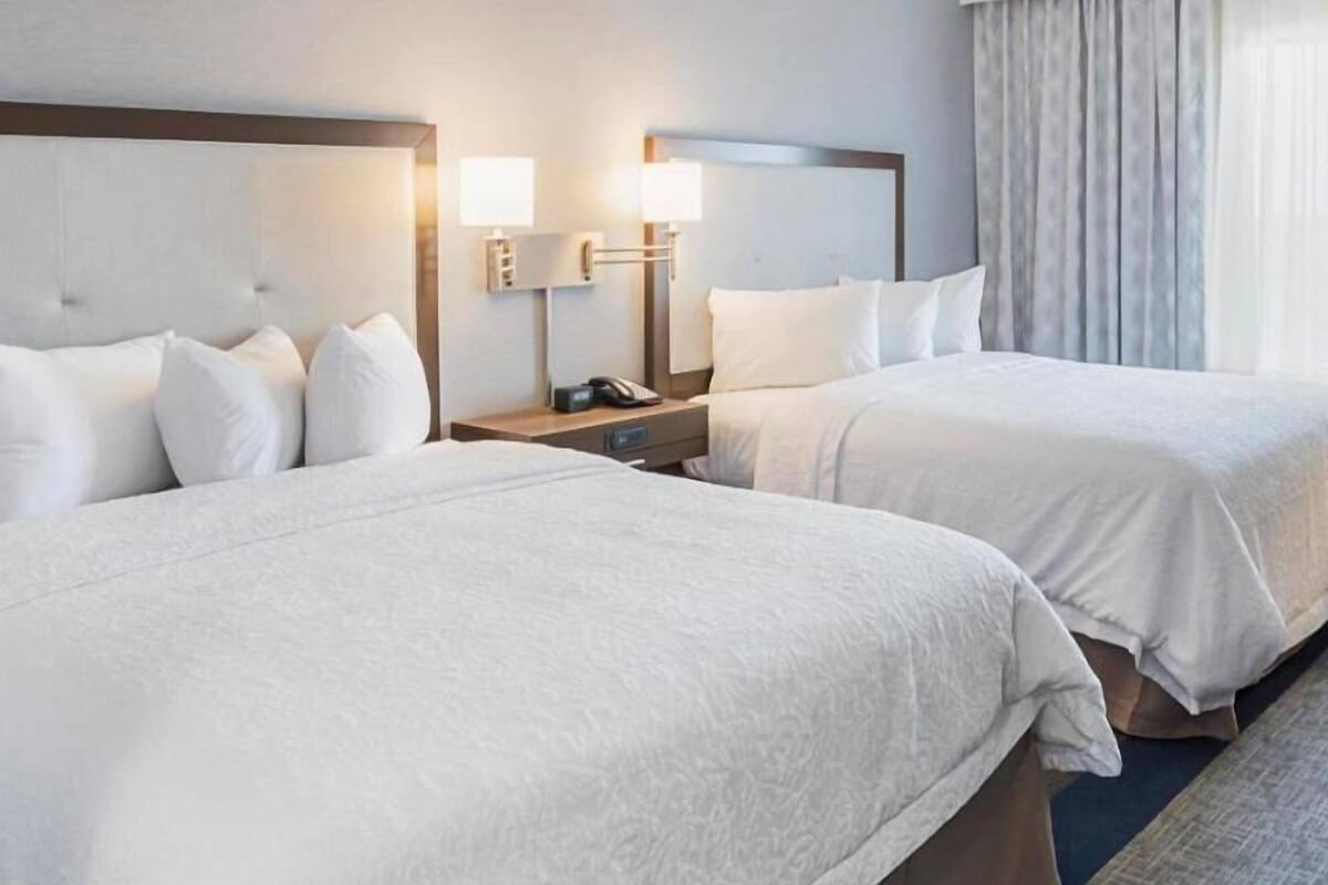 A hotel room with two beds, a nightstand with a lamp, and a window with curtains.