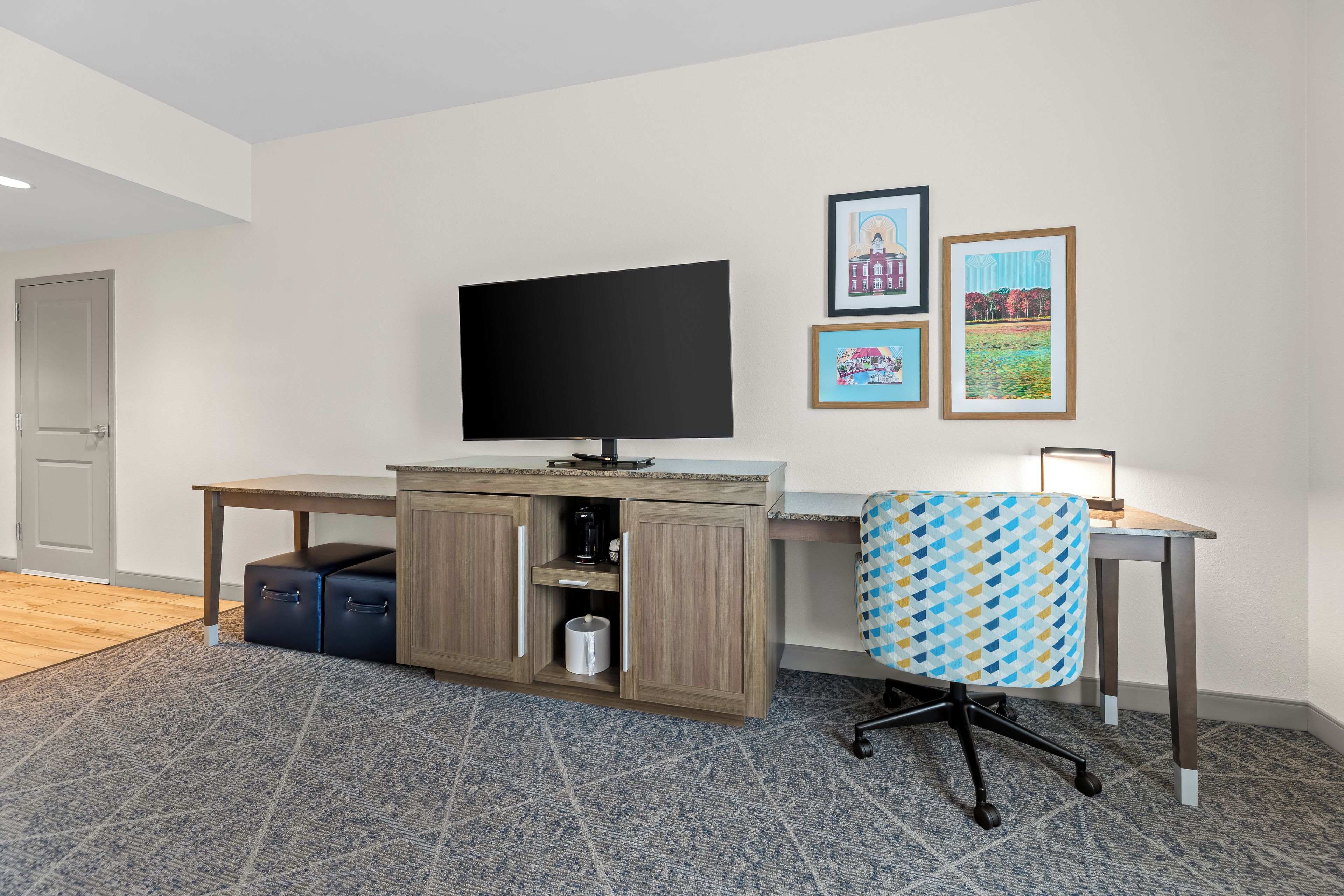 A modern office space with a flat-screen TV, a desk, a chair, and a coffee machine.