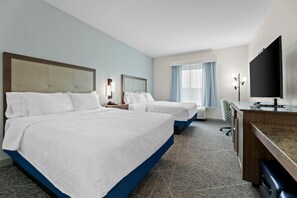 A hotel room with two beds, a desk with a flat-screen TV, a desk lamp, and a window with curtains.