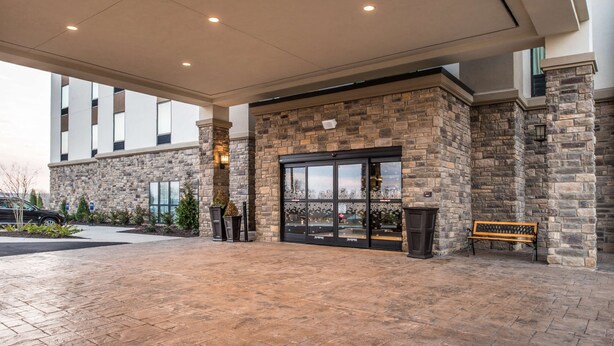A building entrance with a stone facade, large glass doors, and a covered area with a bench. - Hampton Inn Paragould (Paragould)