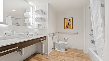 A modern bathroom with a white sink, mirror, and toilet, wooden floor, and a shower curtain.