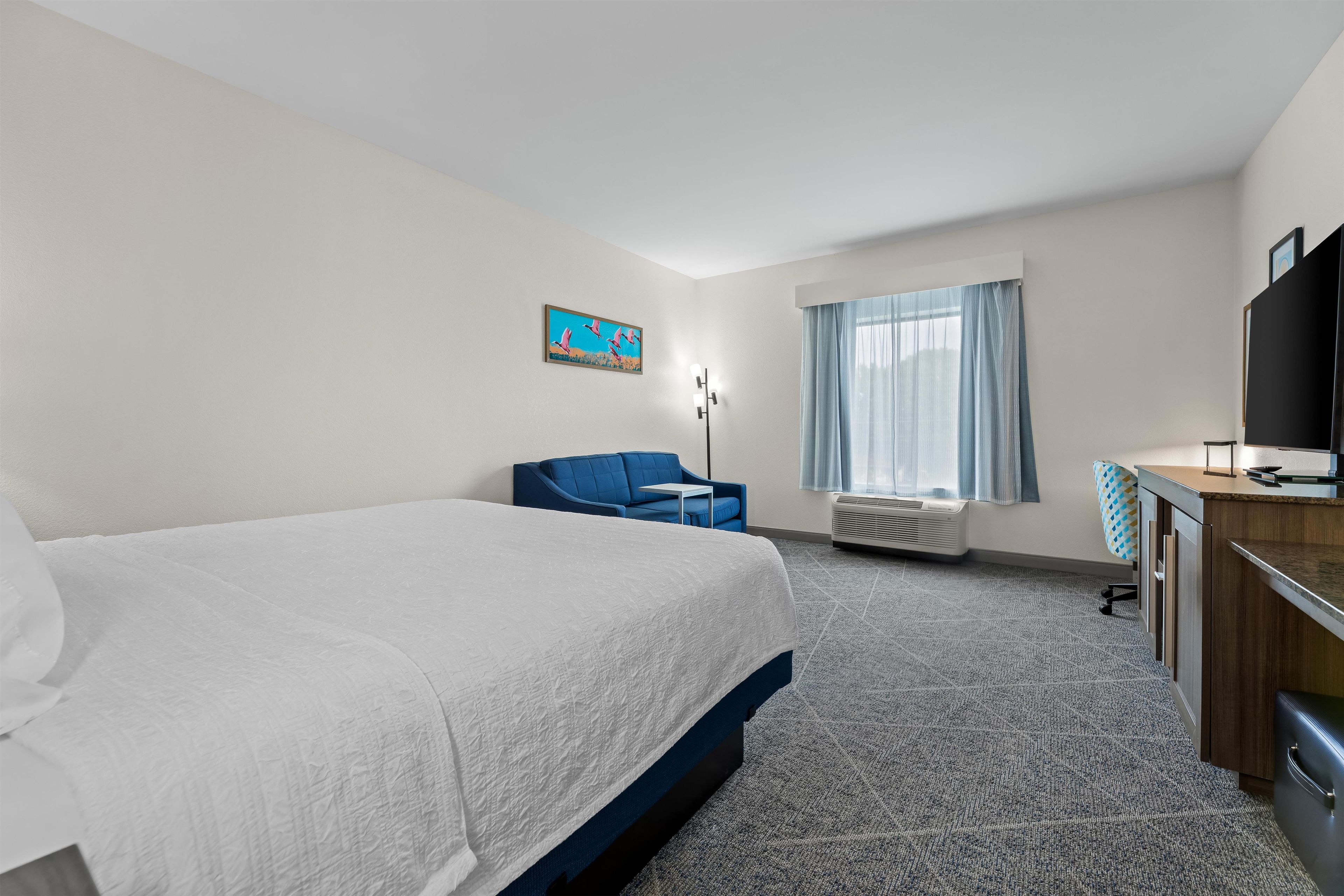 A hotel room with a large bed, a desk, a chair, a television, and a window with curtains.