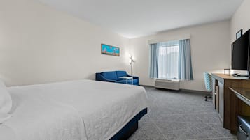 A hotel room with a large bed, a desk, a chair, a television, and a window with curtains.