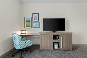Una habitación con escritorio, silla, televisor y cuadros en la pared.