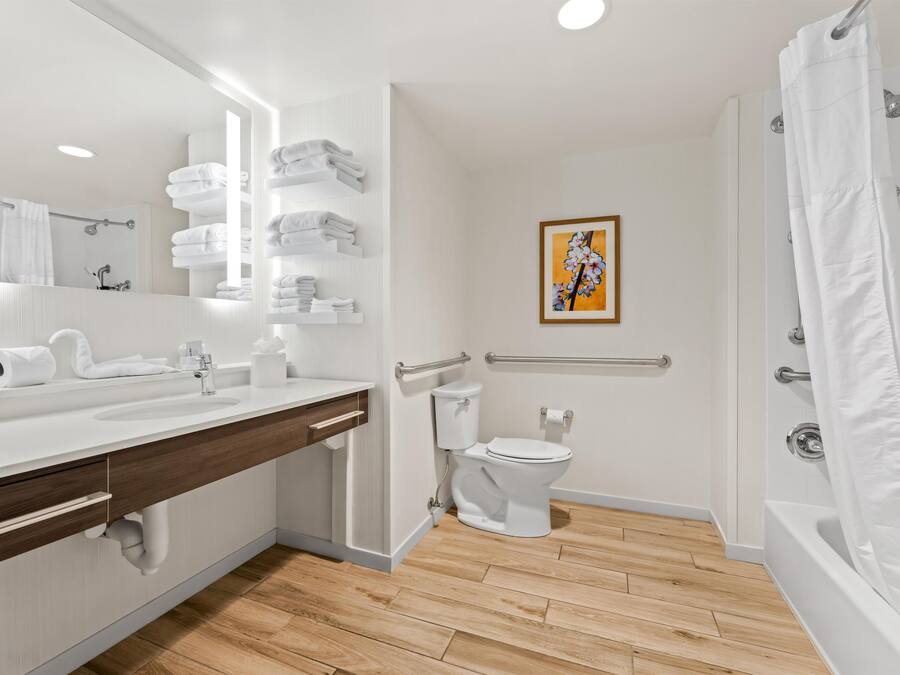 Un baño moderno con un lavamanos blanco, espejo y retrete, suelo de madera y cortina de ducha.