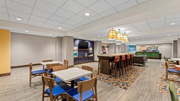 Un hall d’hôtel comprenant un bar, des espaces aménagés avec des sièges et un comptoir de réception.