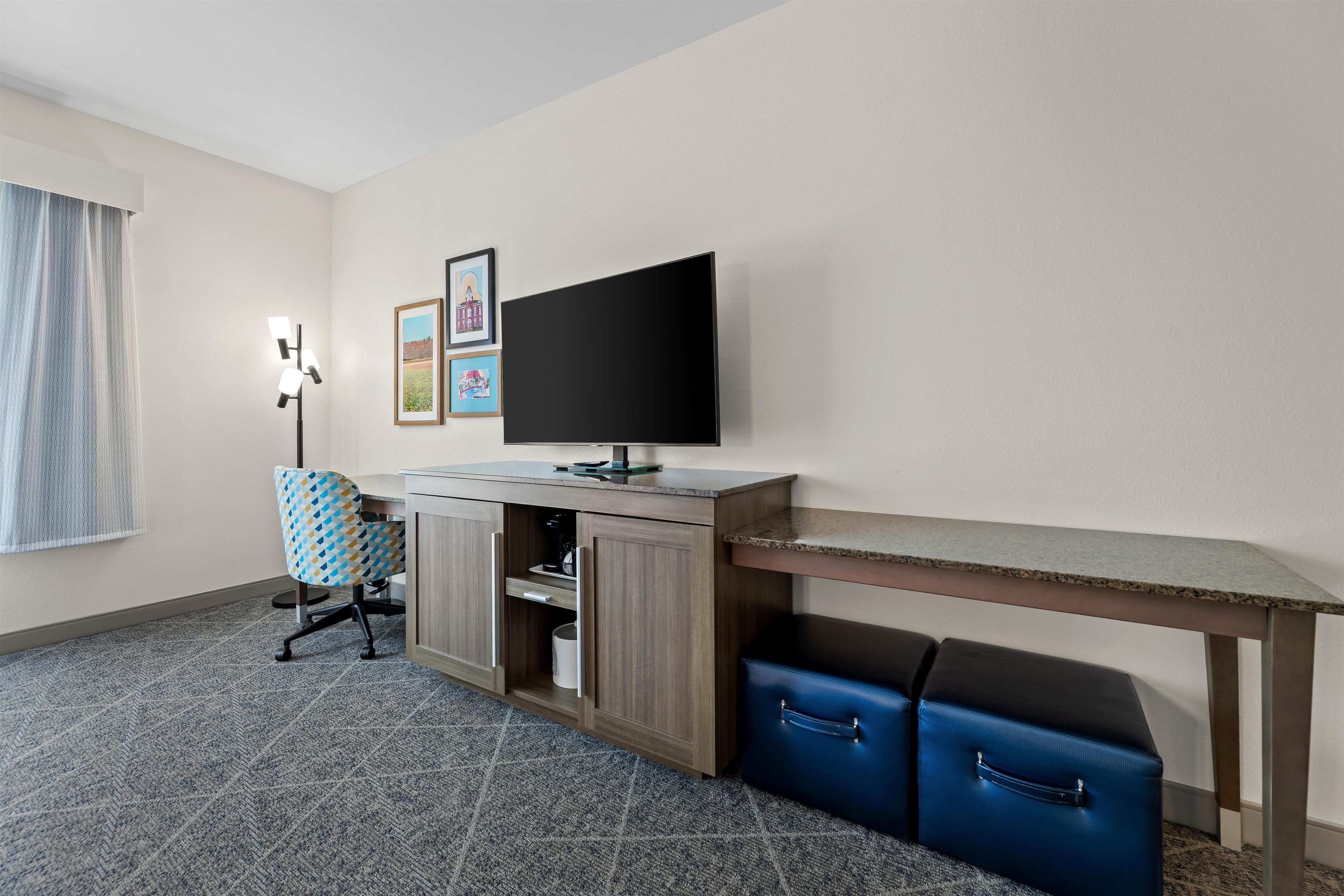 A hotel room with a desk, a television, a chair, a wardrobe, and a suitcase.