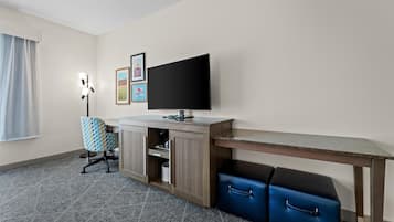 A hotel room with a desk, a television, a chair, a wardrobe, and a suitcase.