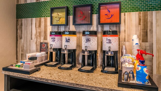 A coffee station with four dispensers, a menu board, and various coffee-related items.