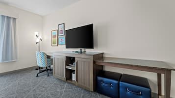 Habitación de hotel con escritorio, televisión, silla, armario y maleta.