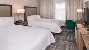 A hotel room with two beds, a desk, a chair, and a television.