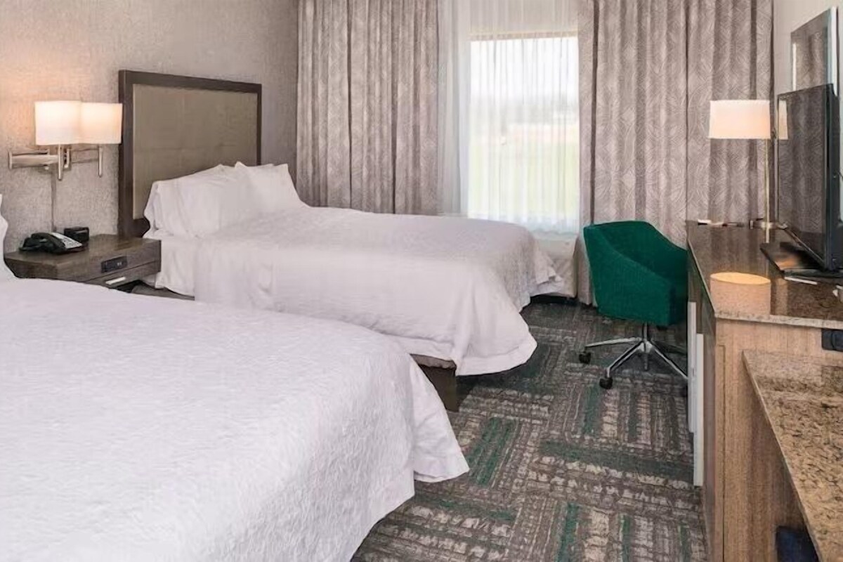 A hotel room with two beds, a desk, a chair, and a television.