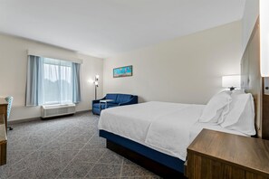 A hotel room with a large bed, a blue armchair, a painting on the wall, and a window with sheer curtains. - Hampton Inn Paragould (Paragould)