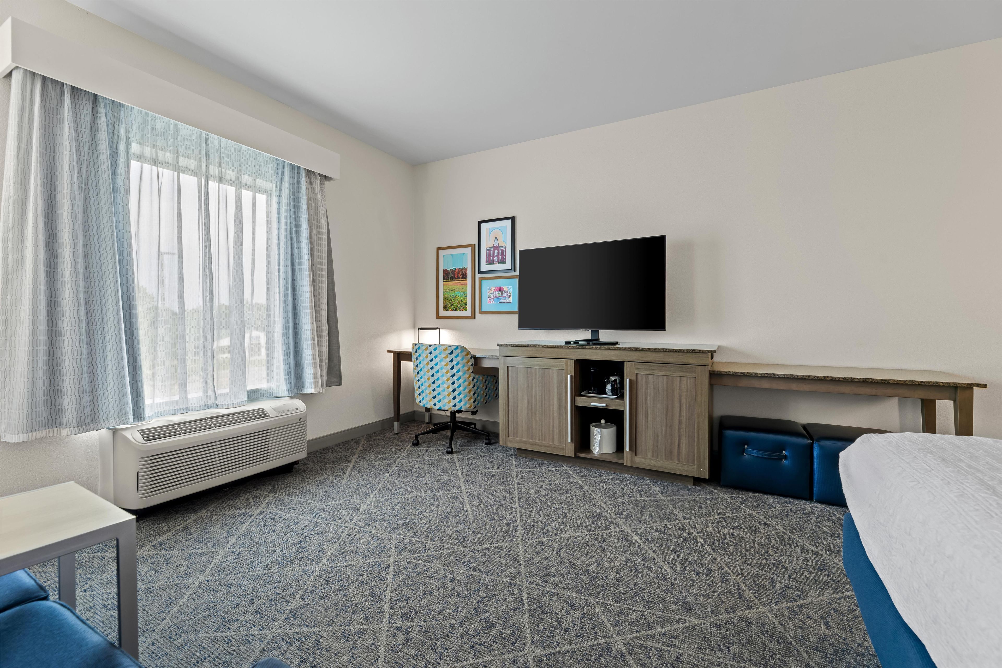 A hotel room with a bed, a desk, a chair, a television, and a window with curtains.