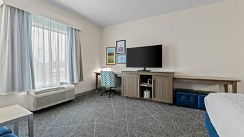 A hotel room with a bed, a desk, a chair, a television, and a window with curtains.