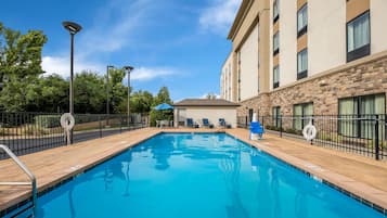 A swimming pool with a wooden deck, lounge chairs, and a building with stone facade.