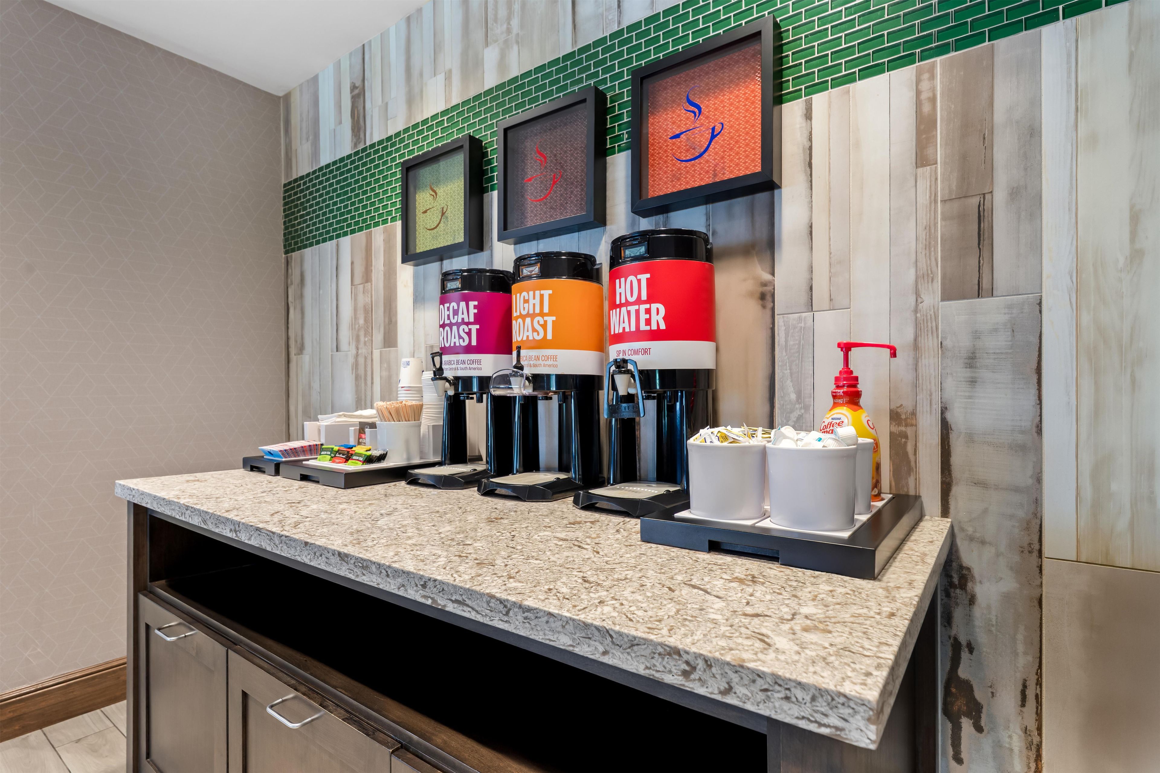A coffee station with labeled dispensers for decaf roast, light roast, and hot water.