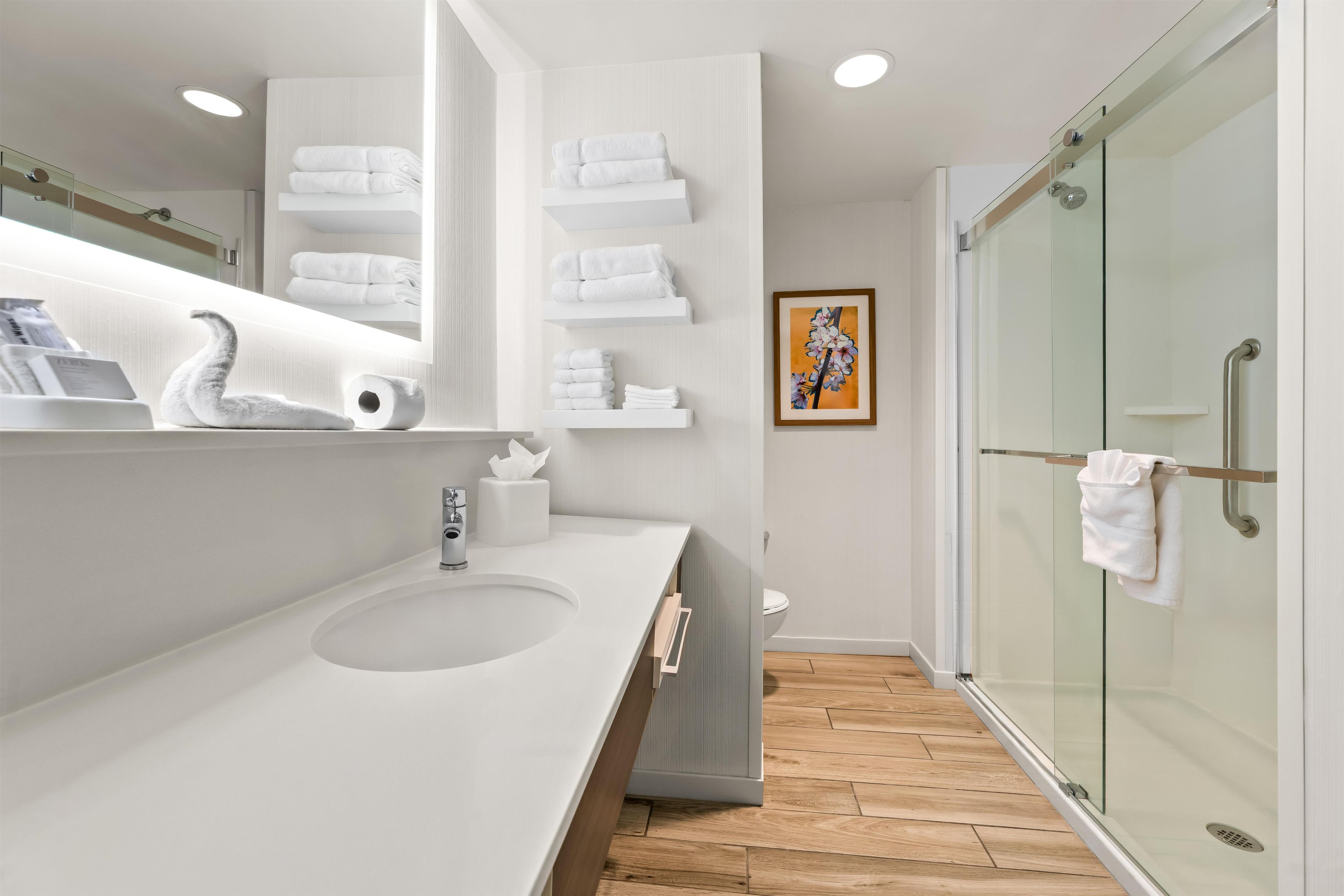 A modern bathroom with a large mirror, a sink, and a glass shower enclosure.
