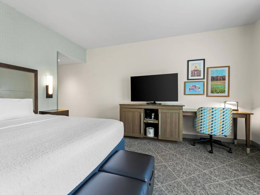 A hotel room with a bed, a desk, a television, and artwork on the wall.