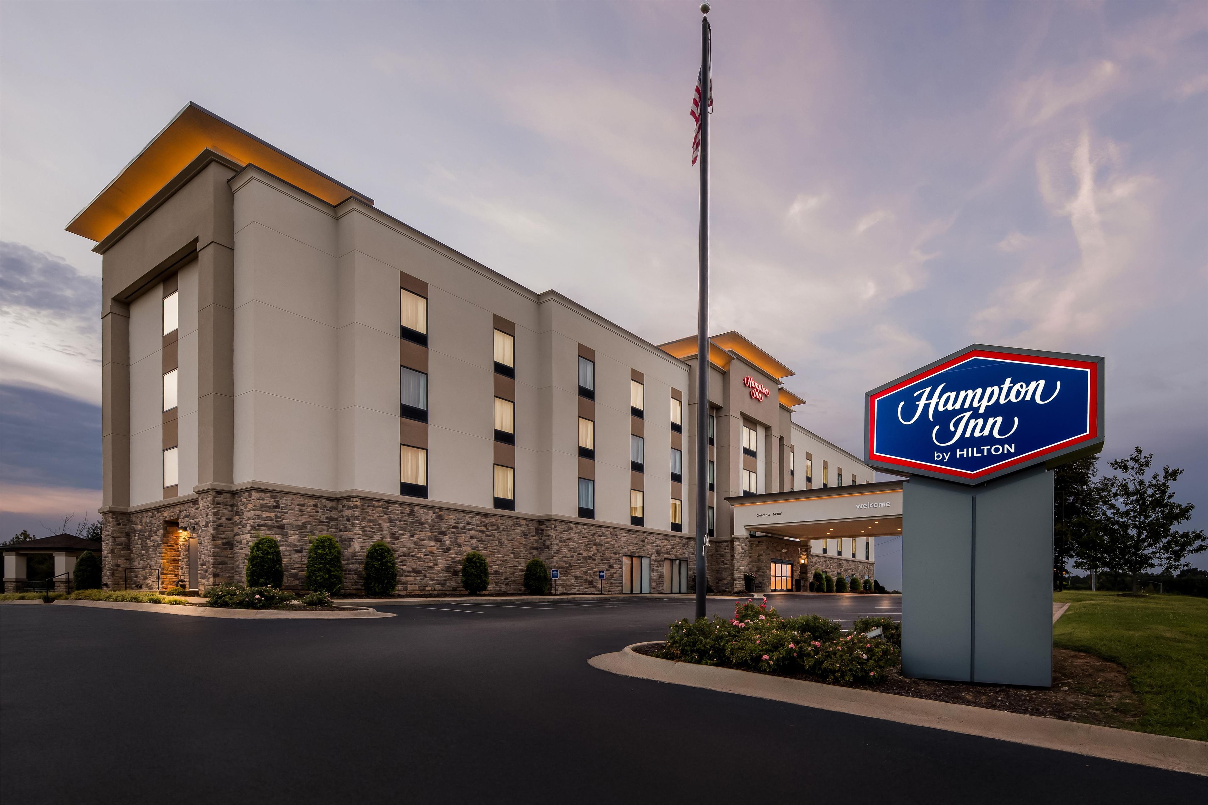 Un hotel Hampton Inn by Hilton con fachada de piedra, varias ventanas y una bandera estadounidense.