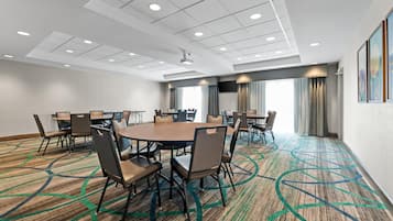 A conference room with a large oval table surrounded by chairs, a flat-screen TV mounted on the wall, and a patterned carpet.